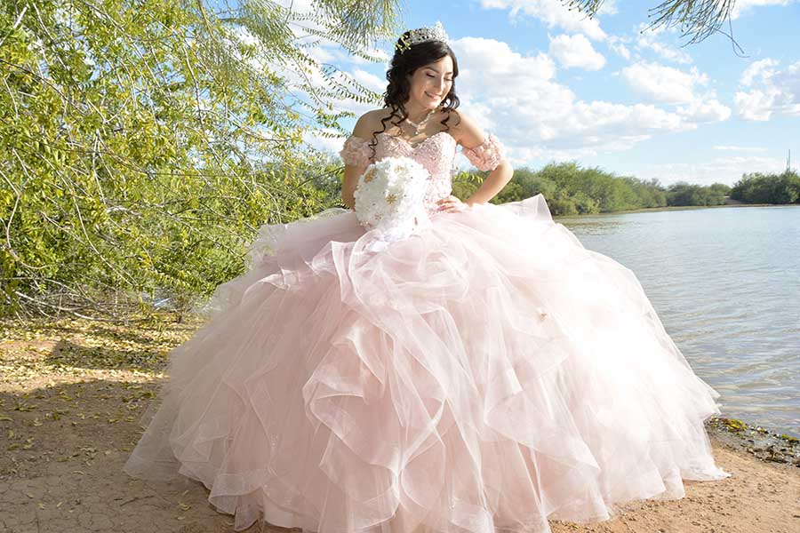 Quinceañera con vestido rosa y tiara posando junto a un lago al aire libre, fotografía de AZ Foto y Video / IAZ Photo Studio.