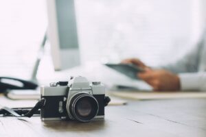 Cámara fotográfica vintage sobre un escritorio, con una persona desenfocada revisando documentos al fondo.