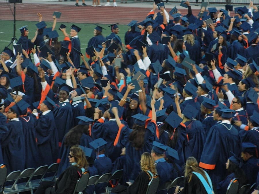 Multitud de estudiantes con toga y birrete celebrando una graduación en un estadio, levantando diplomas y gorras al aire, foto de AZ Foto y Video / IAZ Photo Studio.