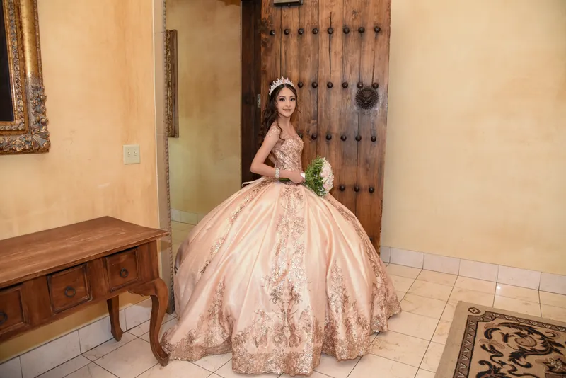 Quinceañera con vestido color durazno brillante y tiara posando con ramo en puerta. Fotografía profesional en Gilbert AZ.